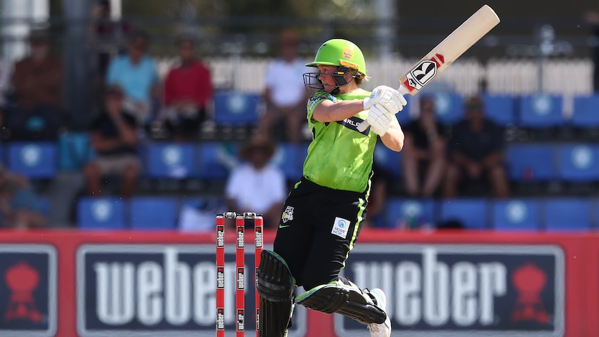 Corinne Hall wears her lime green Thunder kit and balances one leg with her bat raised in the air after playing a shot