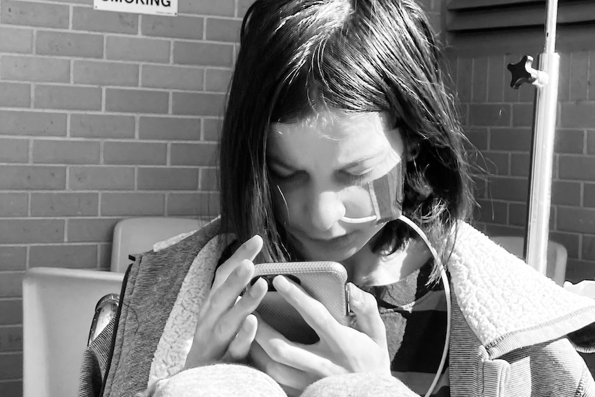 A young person with a feeding tube down their nose looks at a smartphone.