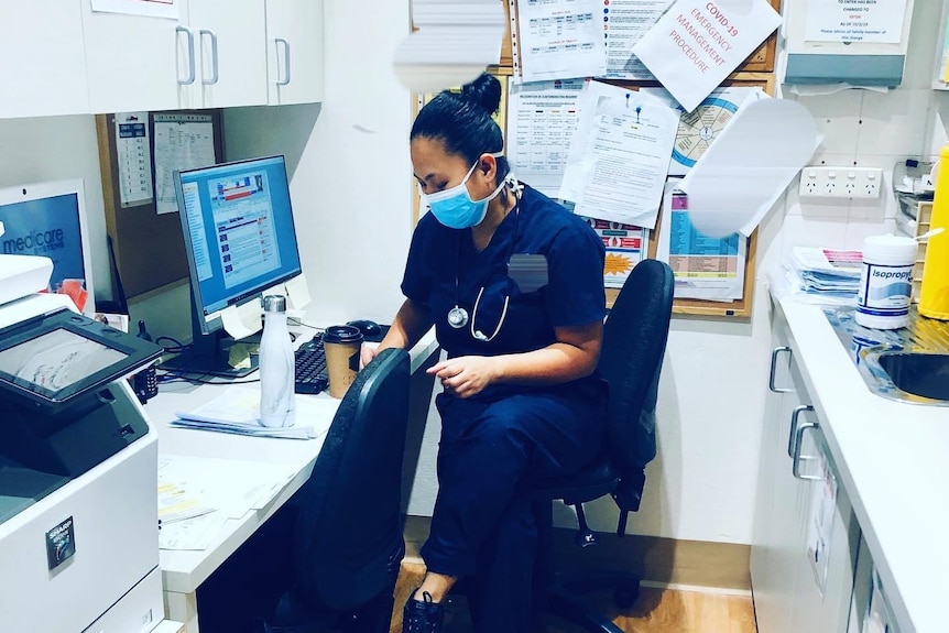 Judy Ann Imperial sitting at her desk, wearing her uniform and a mask. 