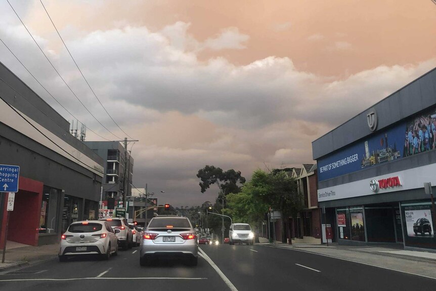 The sky is an eerie pale orange as cars drive down a suburban road in Melbourne.