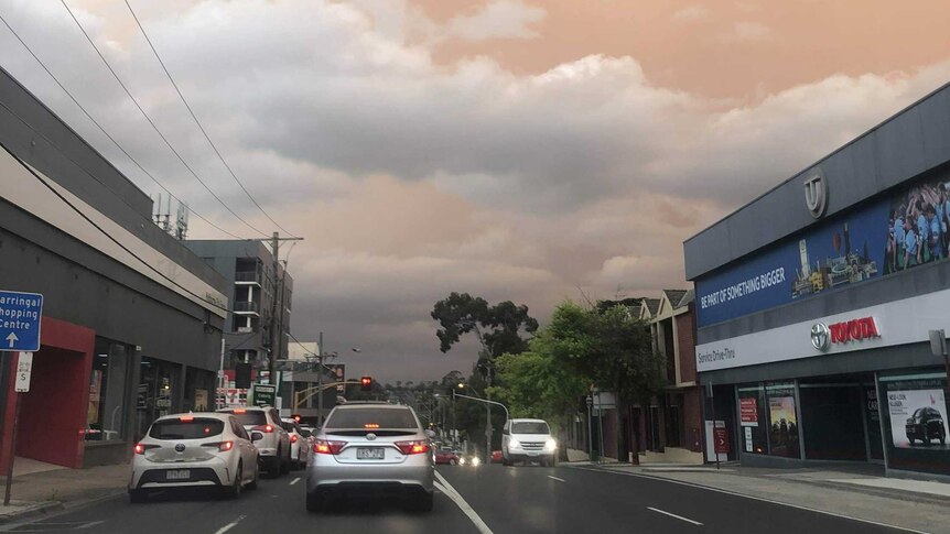 The sky is an eerie pale orange as cars drive down a suburban road in Melbourne.