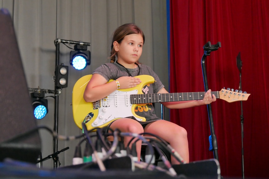 A young girl with a yellow guitar on a stage