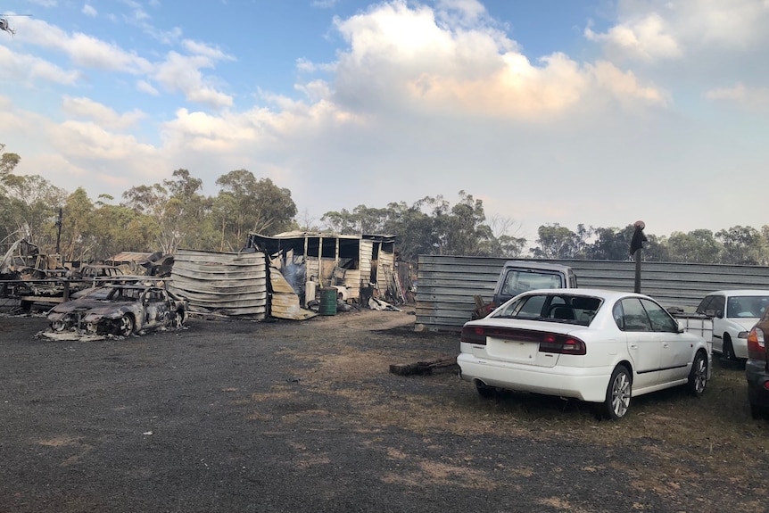 A burnt out car in front of a building also damaged by fire.