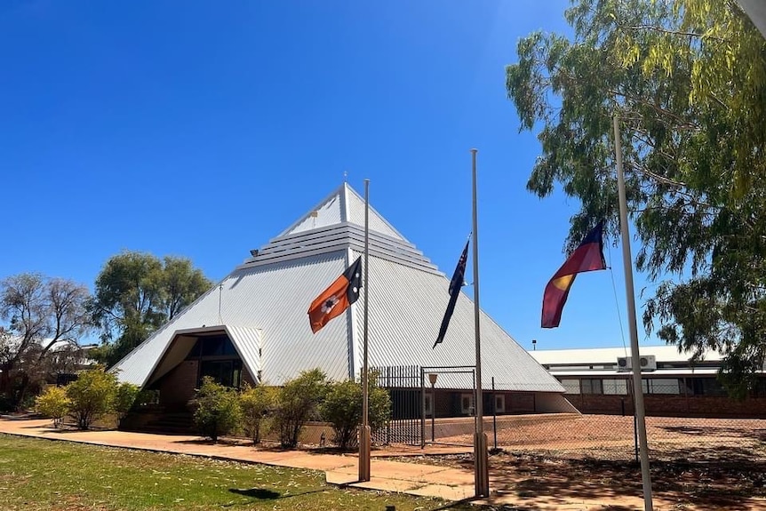 A pyramid shaped building with three flags out the front at half mast.