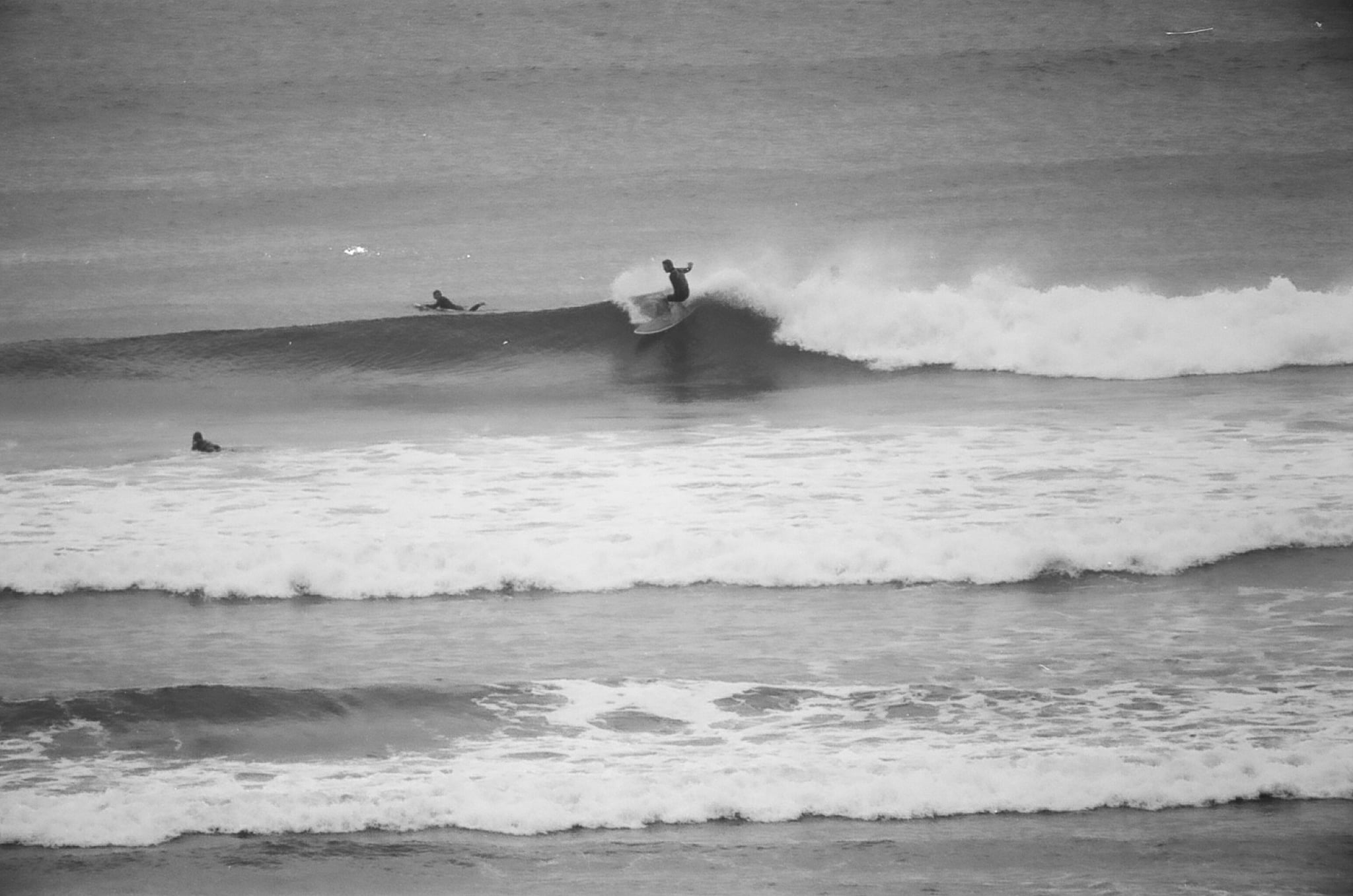 Fotografía en blanco y negro del agua en una playa con un hombre surfeando una ola.
