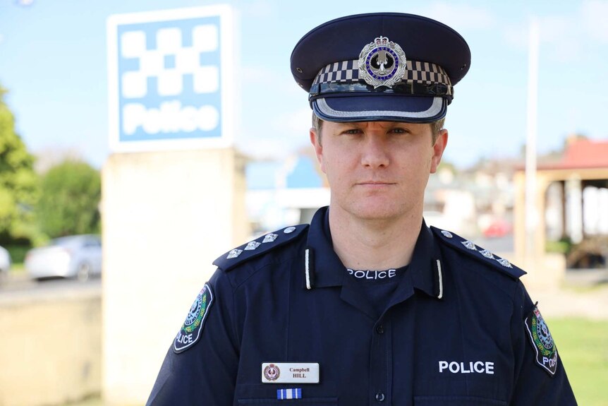A man stands in front of a police sign, wearing a navy blue South Australian police uniform and hat.