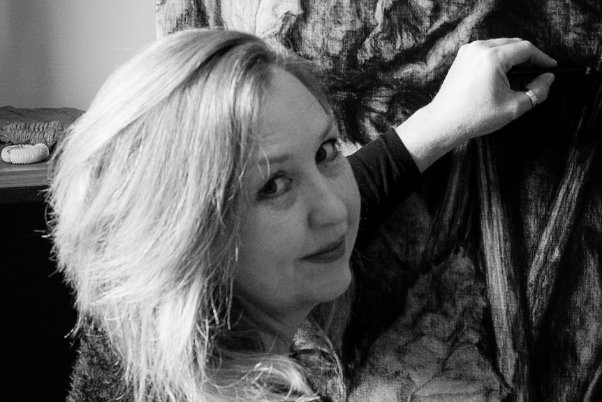 A black and white shot of a blonde woman working on a charcoal drawing.