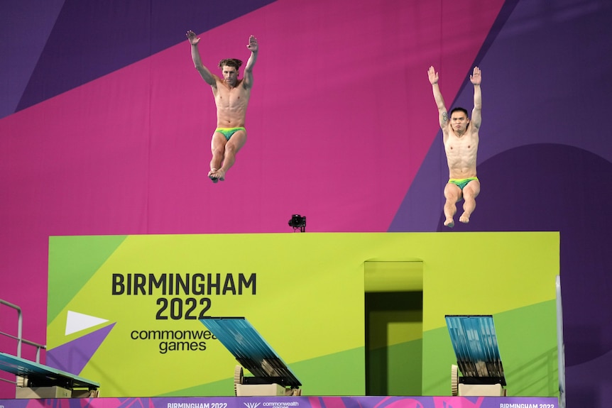 Two male divers jump off a diving board at an event