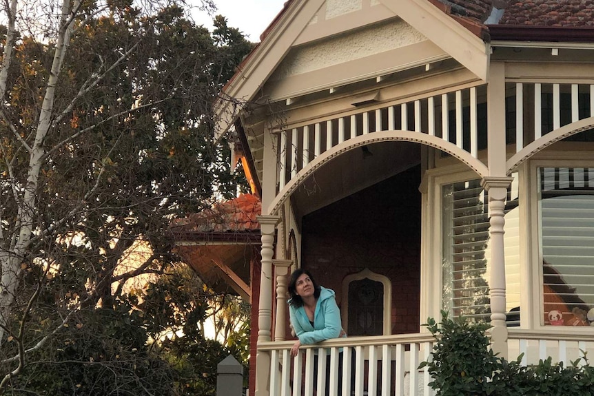 Lisa leans on a veranda, looking up at the sky.