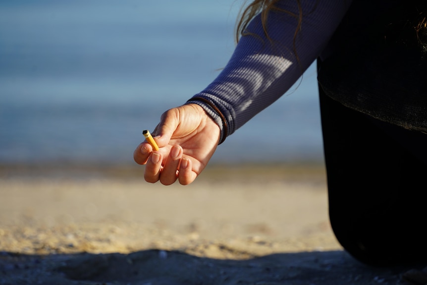 A woman's hand holding a cigarette butt on the beach.