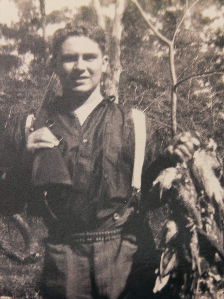Black and white photograph of a man with a gun over his shoulder holding a string of dead birds