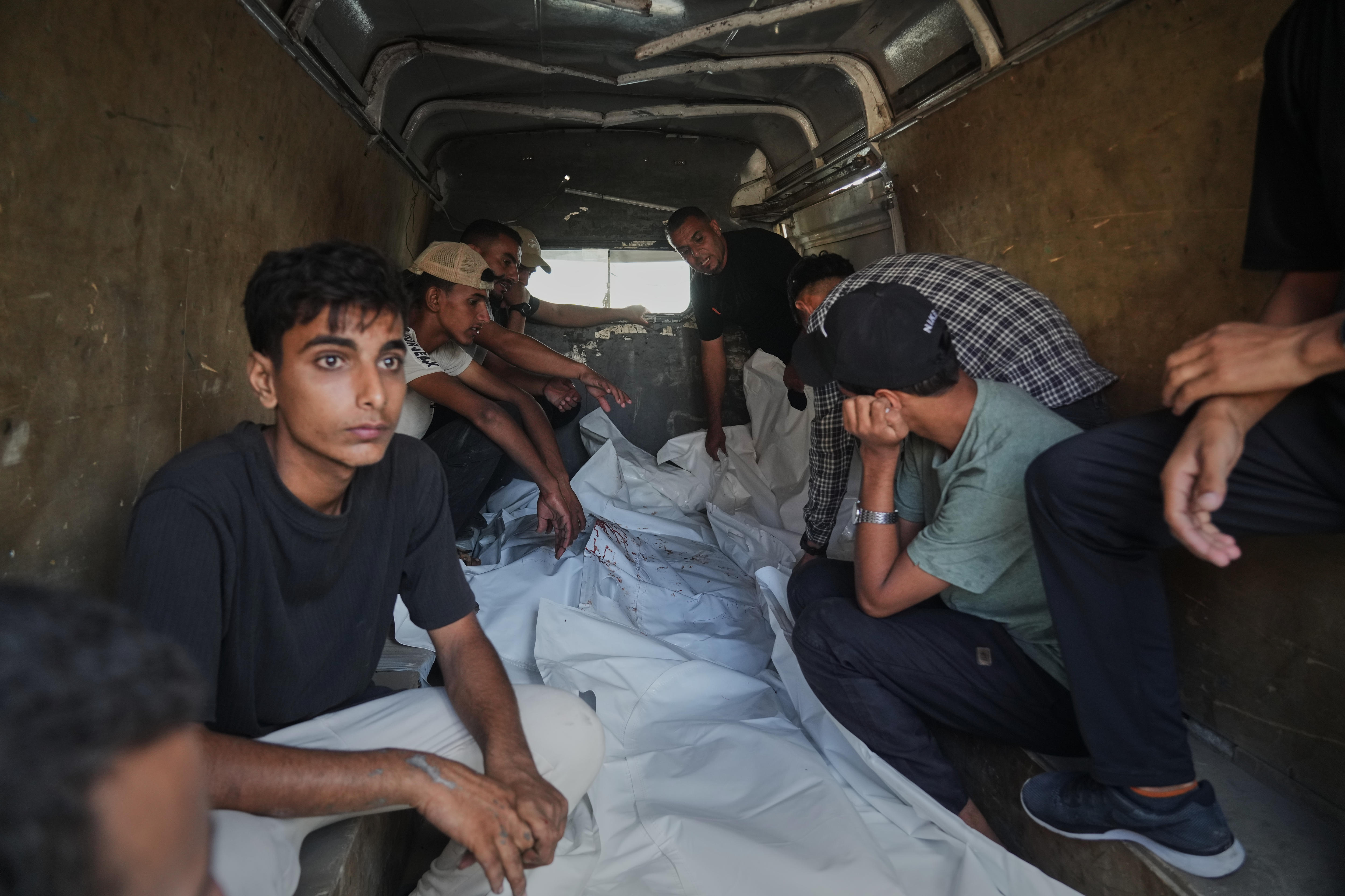 Men sitting inside a van around a body covered in a white sheet.