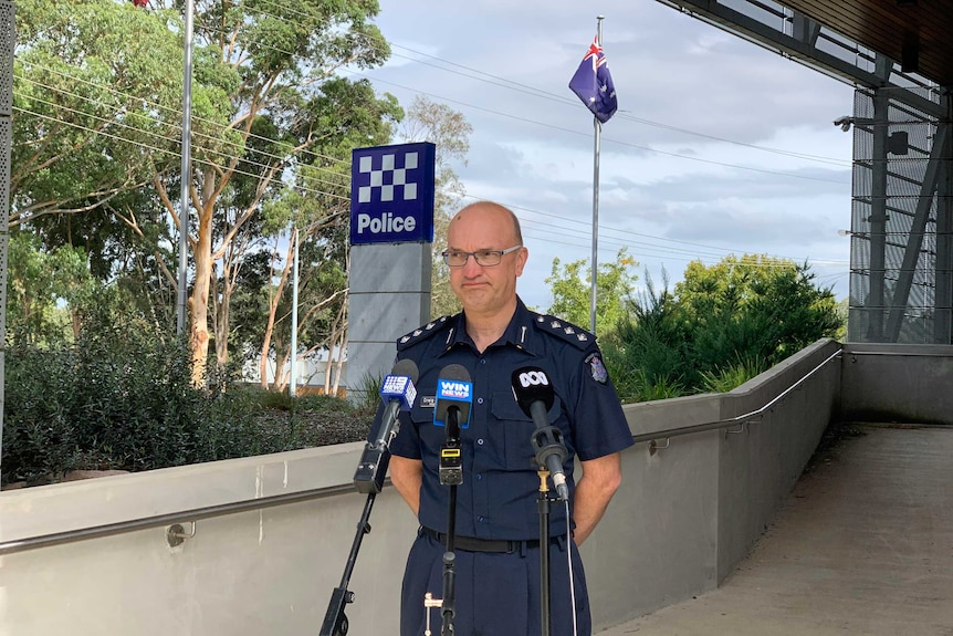 A middle-aged man in a police uniform standing in front of the media pack.