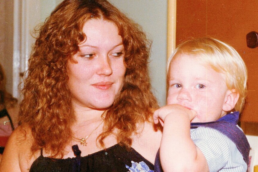 An old photo shows a young woman holding a blonde toddler in her arms.
