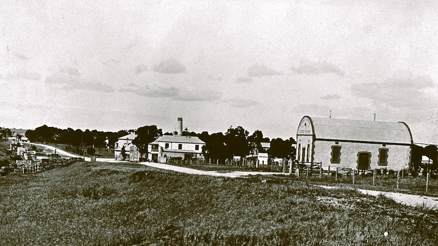 A black and white photograph showing a building with a barrel roof next to a road that also runs past 