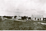 A black and white photograph showing a building with a barrel roof next to a road that also runs past 