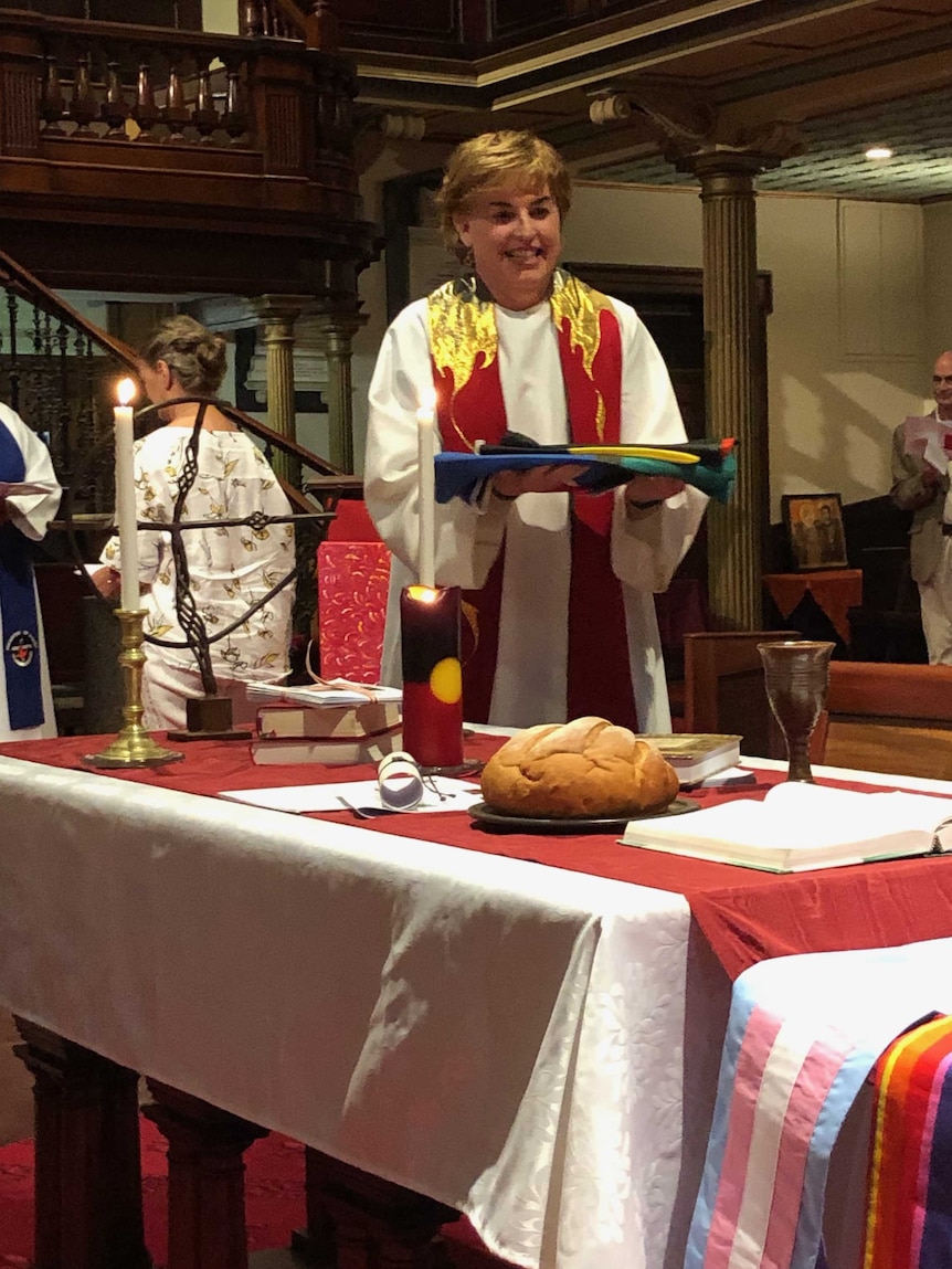 Jo stands behind the church altar, holding a set of fabrics