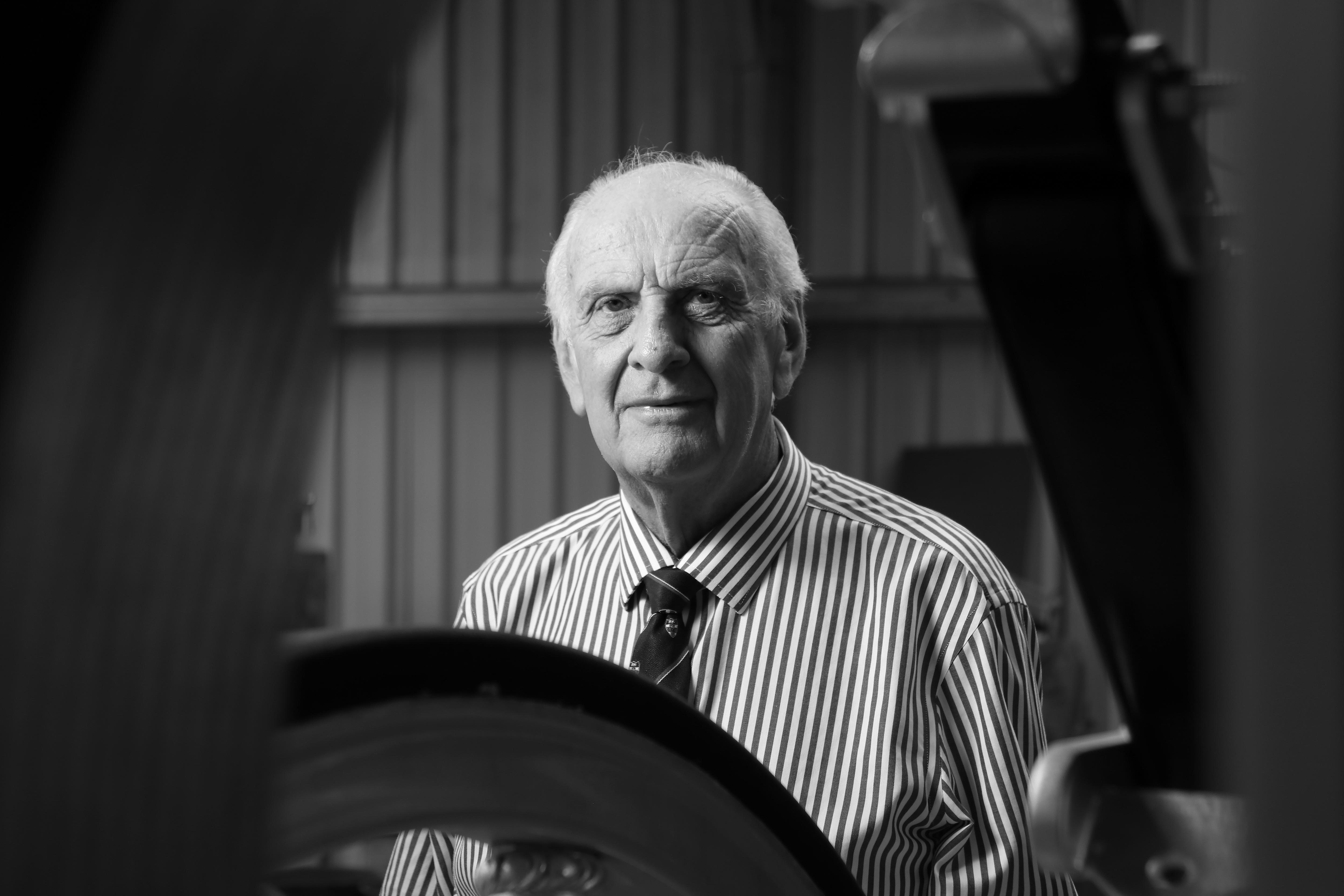 An older, white haired man in striped shirt and tie sitting in a shed.