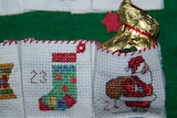 A chocolate bunny in a gold wrapper peeps out of a pocket on a cross stitched advent calendar