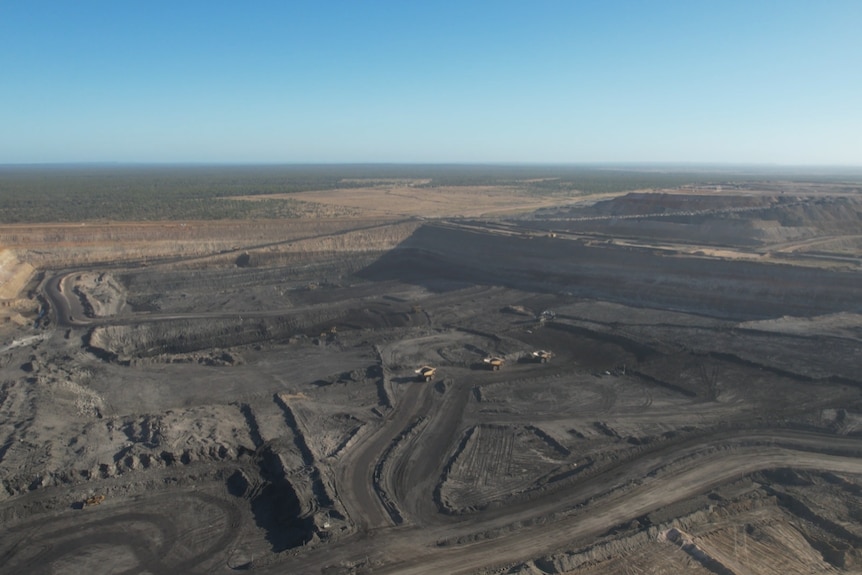 An expanse of black coal being mined in an open-cut pit, among green fields spanning off into the distance.