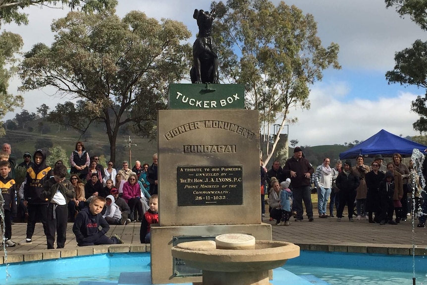 The statue of the dog in the tucker box with a crowd of people behind it.