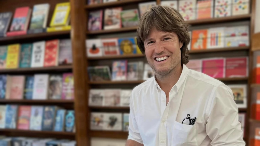 man smiling in white shirt with spectacles in top book in a book shop signing books