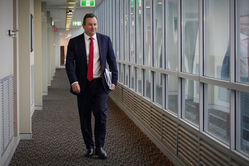 A man in a suit and red tie walks down a hallway