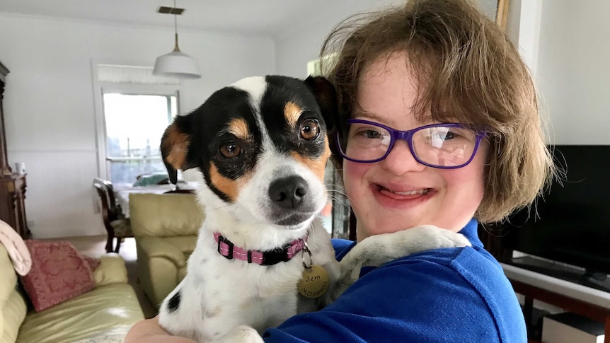 Close up shot of Chiara Casalaz, 18, with a big smile, wearing glasses and hugging a small dog