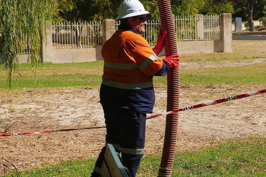 A worker holding an industrial pipe leading into the ground