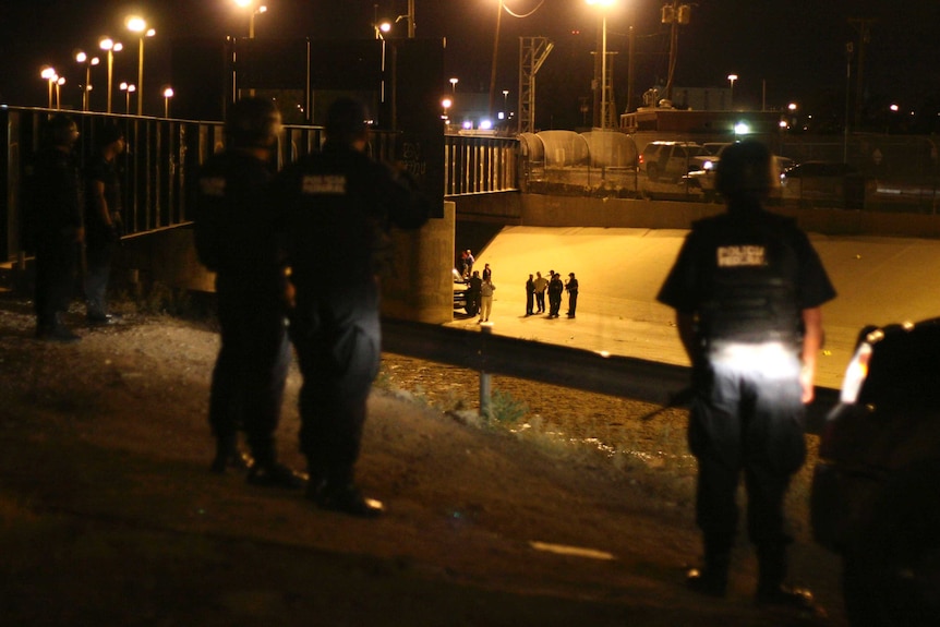Mexican police watch as US border agents stand in a cement drain between El Paso, US and Ciudad Juarez, Mexico.