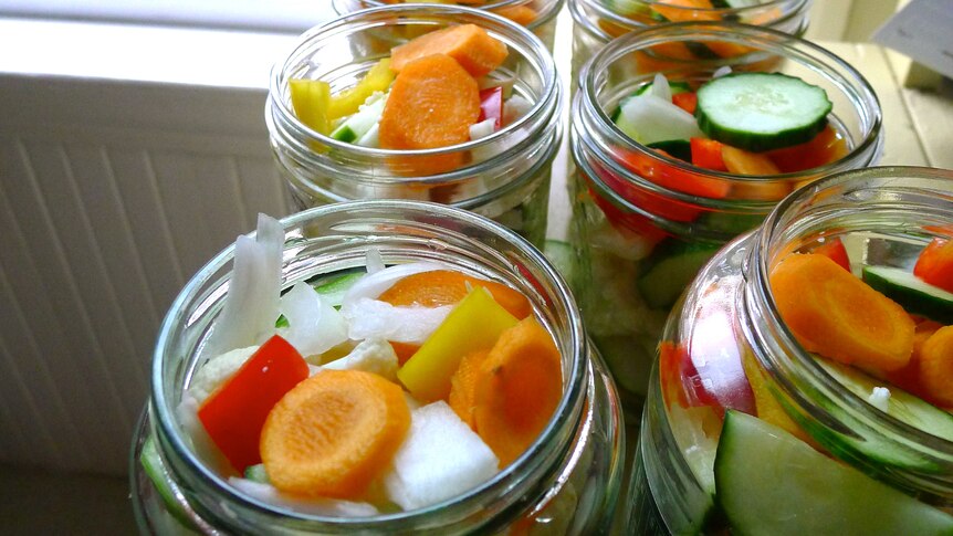 Colourful vegetables chopped in six opened glass jars near a window.