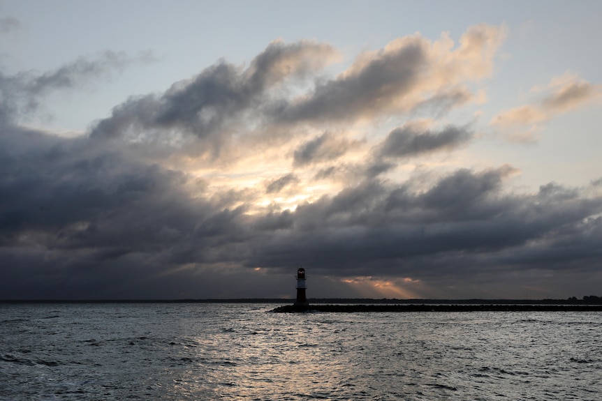 A lighthouse stands at the edge of land, as storm clouds gather over the sea.