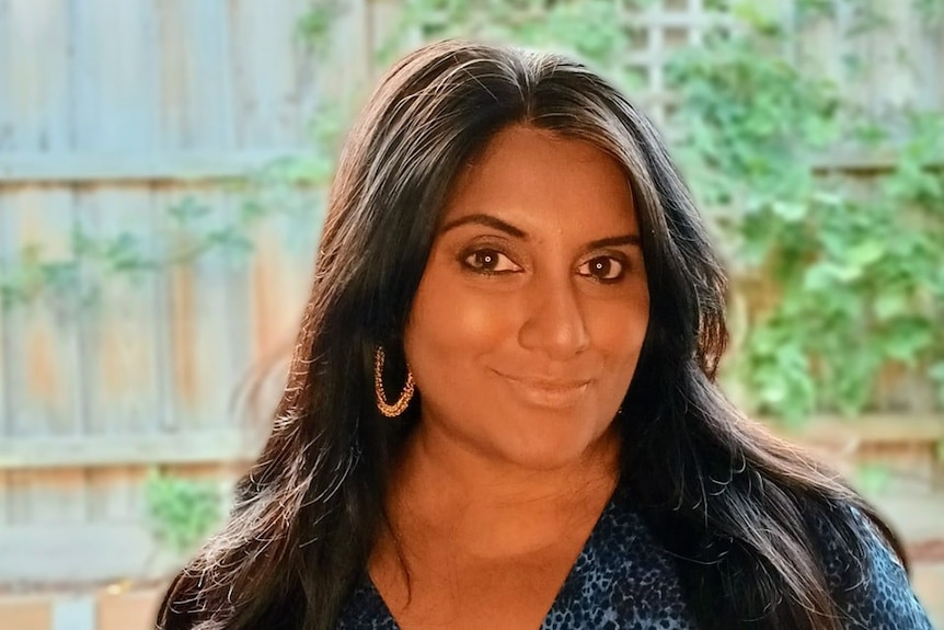 A portrait shot of a South Asian woman with long dark hair wearing a patterned blue blouse.