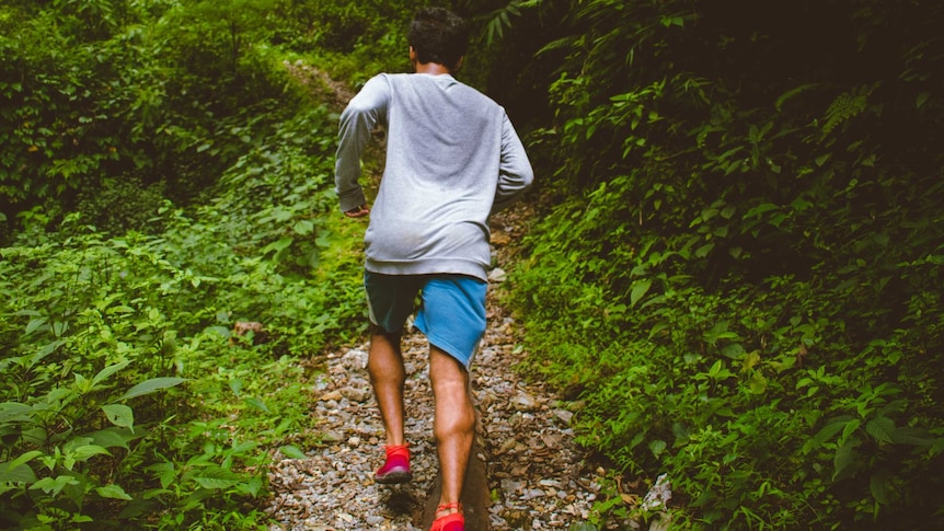 Man runs through forest with a sweaty shirt on.