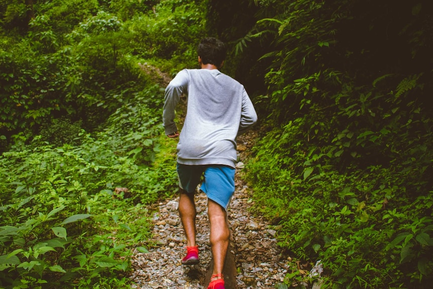 Man runs through forest with a sweaty shirt on.