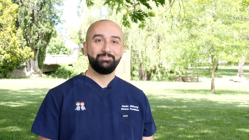 A man in hospital scrubs stands in a park