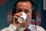 A head and shoulders shot of WA Premier Mark McGowan drinking coffee from a disposable cup in a radio studio.