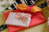Two rectangular shaped presents wrapped in furoshiki fabric: one is red with white dots and the other is purple white flowers