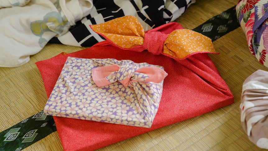 Two rectangular shaped presents wrapped in furoshiki fabric: one is red with white dots and the other is purple white flowers