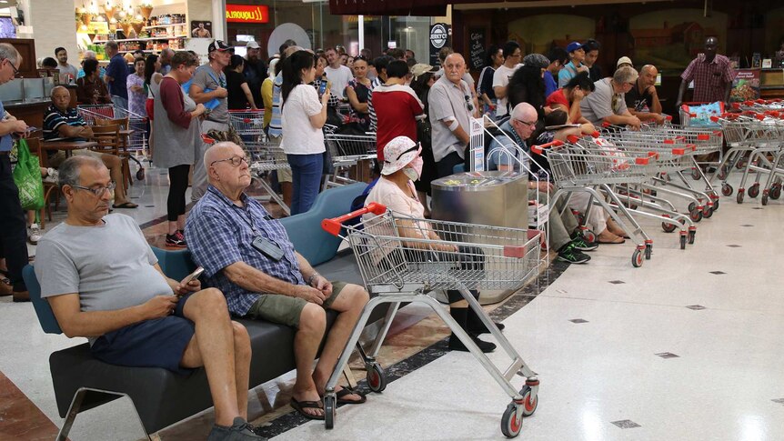 A crowd of shoppers with empty trolleys wait in a shopping centre outside a Miss Maud's store for a Coles store to open.