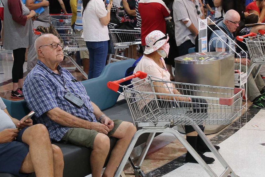 A crowd of shoppers with empty trolleys wait in a shopping centre outside a Miss Maud's store for a Coles store to open.