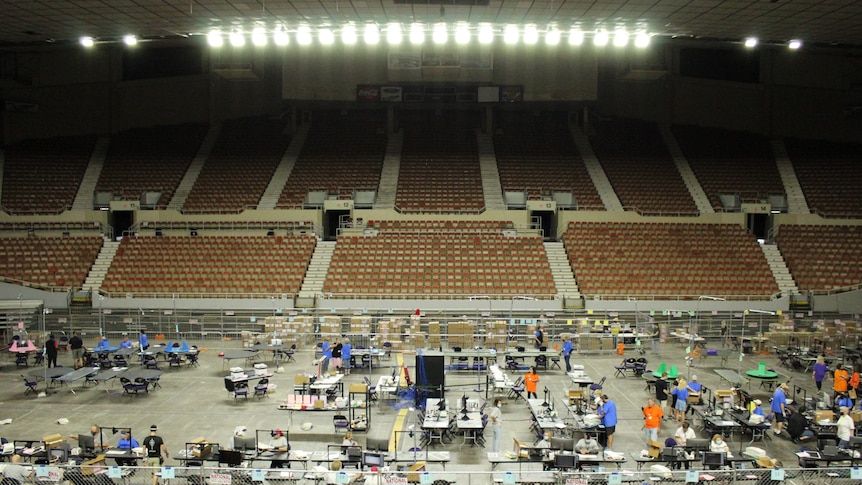 An empty sports arena with cardboard boxes and tables set up on the court 