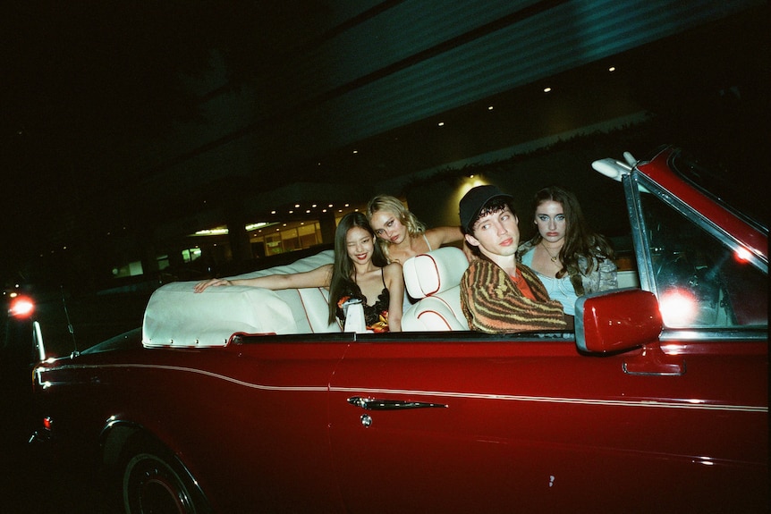 Four people sitting inside a red covertible car at night
