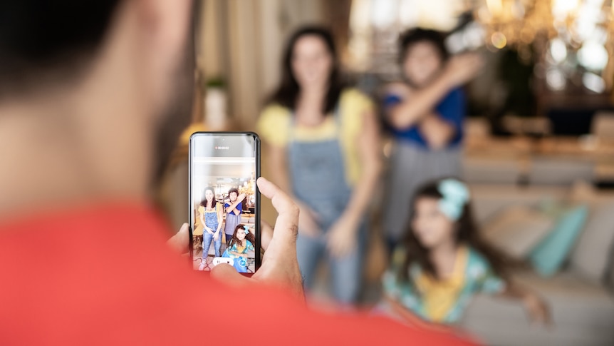 Dad filming or take photo of family dancing at home.