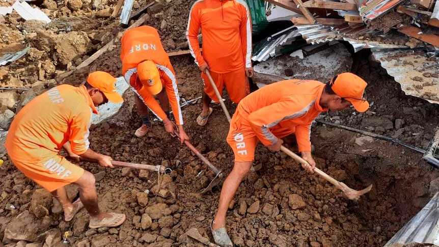 Four men dressed in orange digging through rubble and debris. 