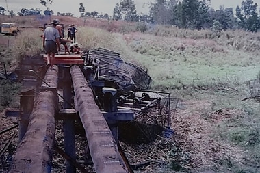 an old photo showing cane bins on top of a train underneath a small bridge 