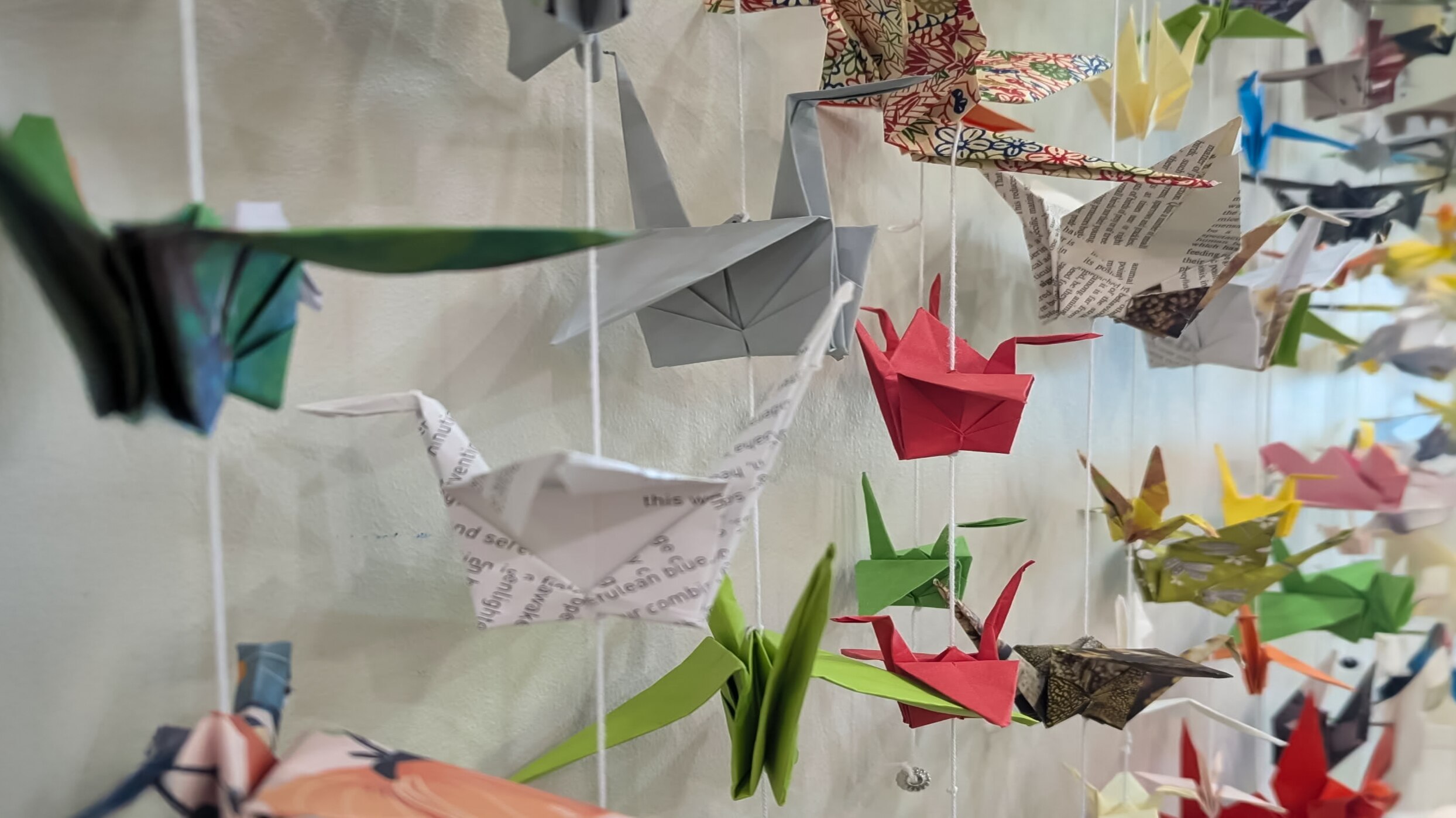 Colourful origami paper cranes hang from the ceiling in a bright gallery.