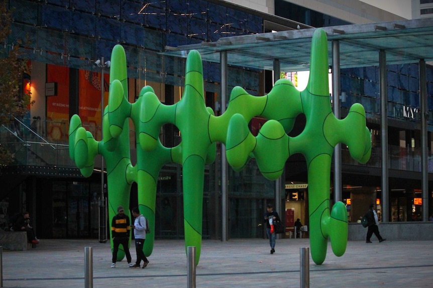 A large green cactus like sculpture sits in the middle of an outdoor shopping mall