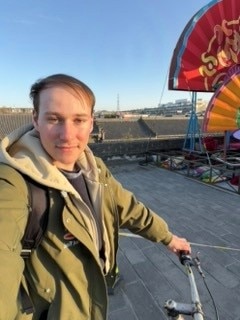 A man rides a bike while on a wall with a bright orange and red installation behind him