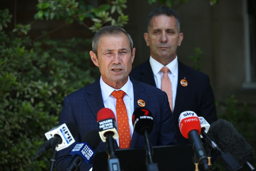 A middle-aged, grey-haired man in a suit – WA Premier Roger Cook – stands outside and speaks to the media.